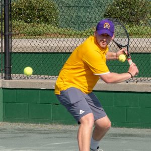 Man playing tennis in yellow shirt and purple hat